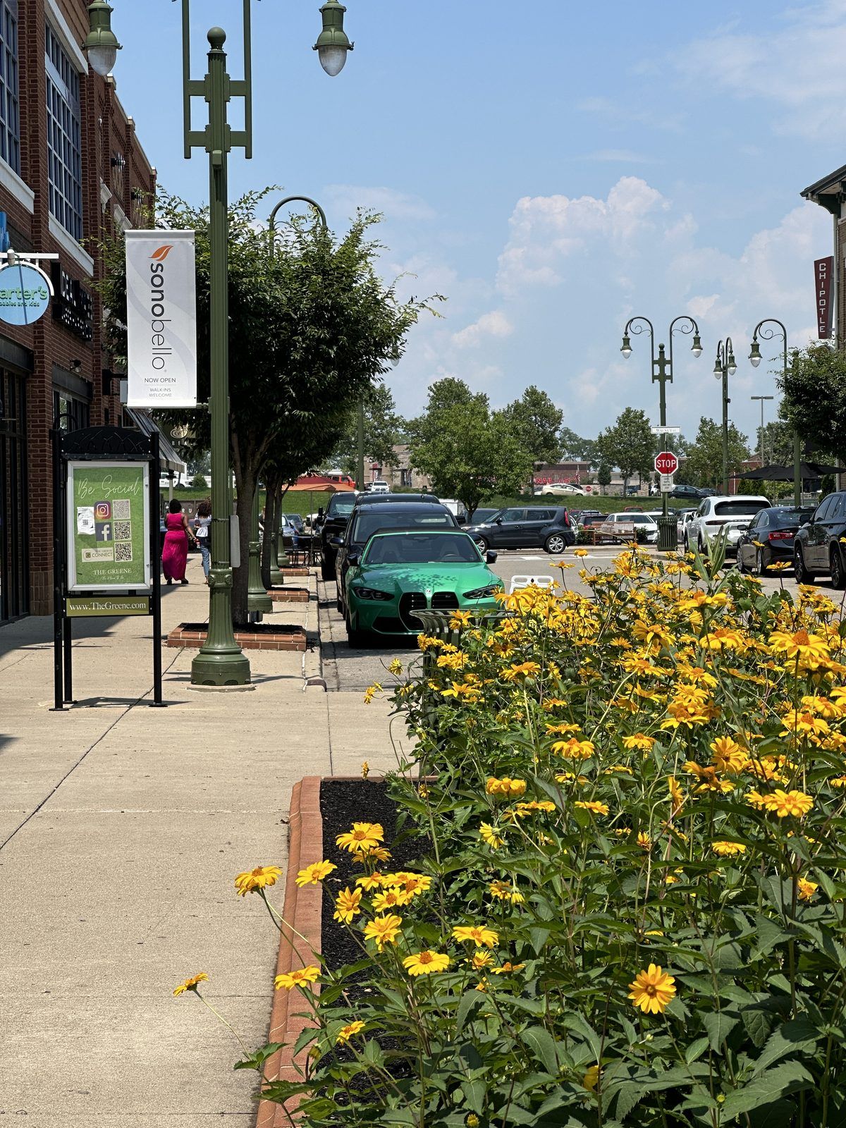 Sunny sidewalk at The Greene with storefronts, lampposts and yellow flowers
